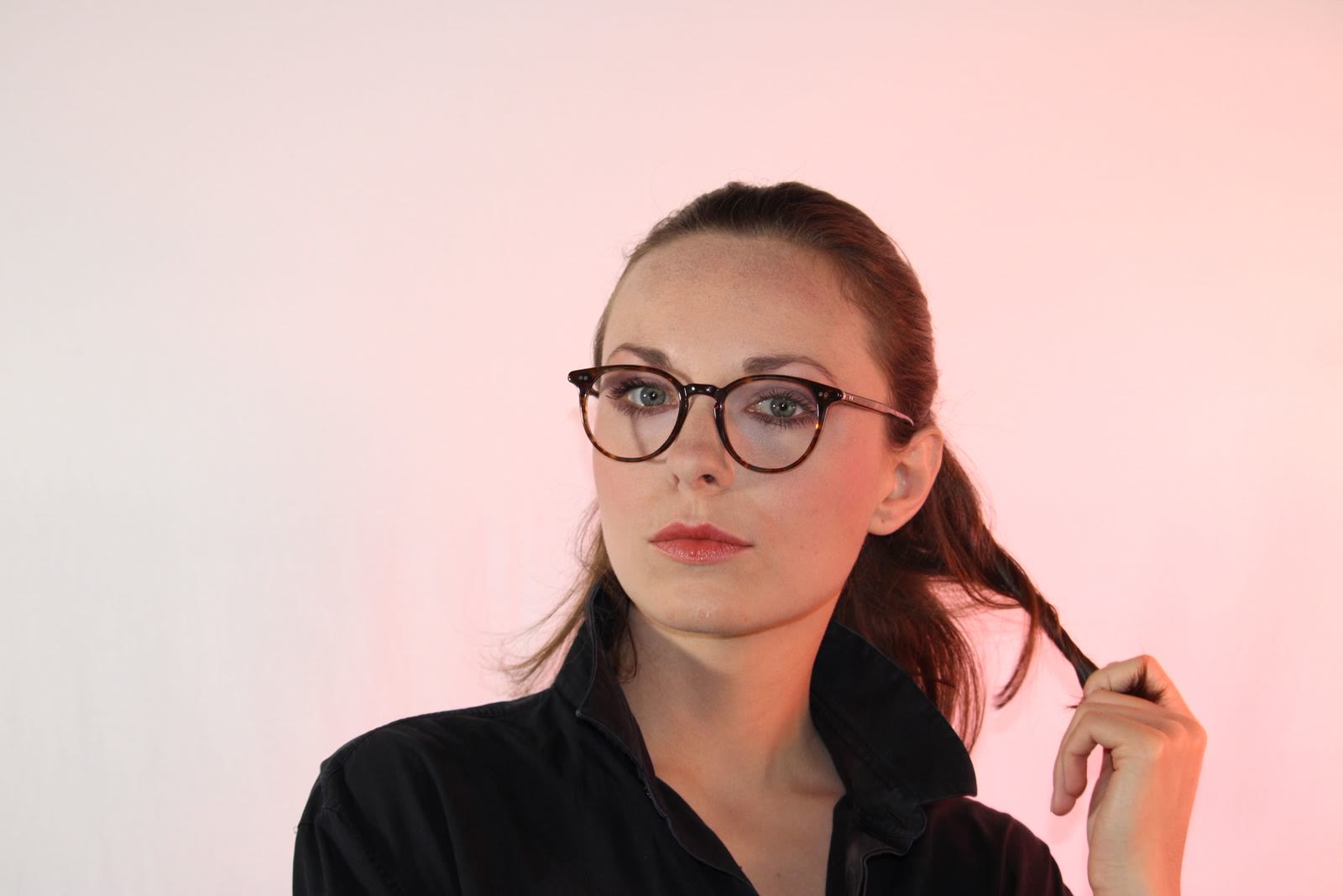 Una donna con occhiali tondi scuri guarda di lato, su un fondo chiaro